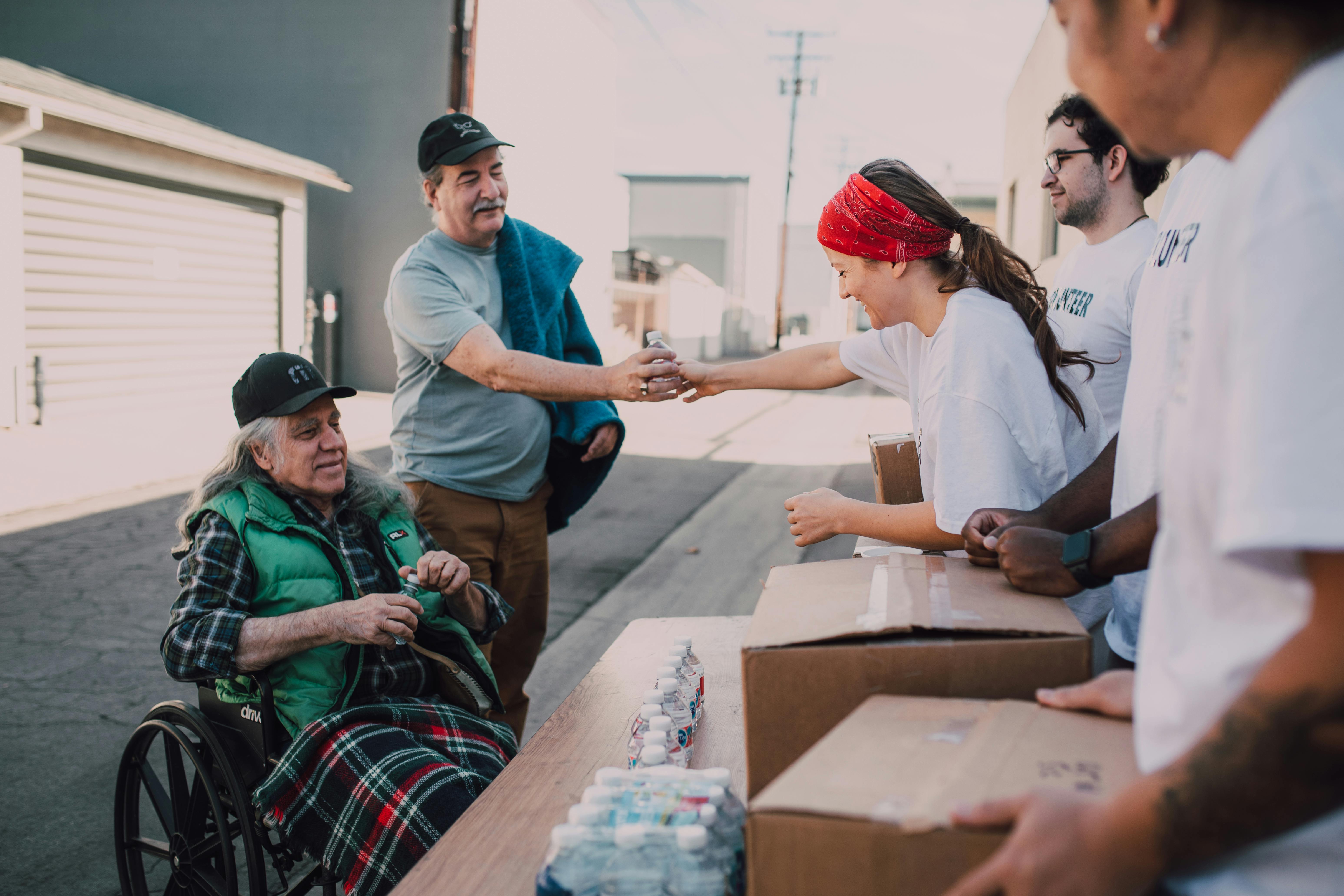 Volunteers distributing supplies to community members including an elderly person in a wheelchair